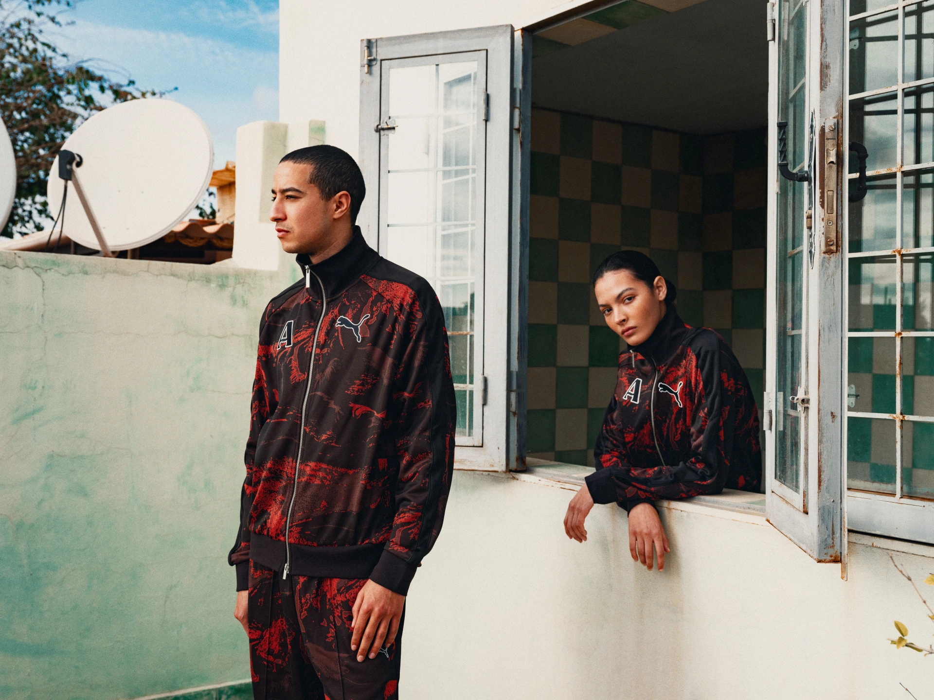 Two models in red and black patterned tracksuits in front of a window