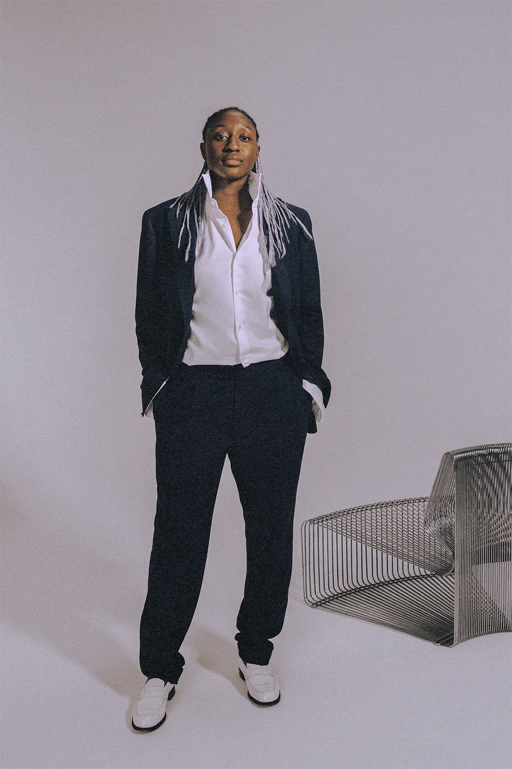 Kadidiatou Diani standing in a suit and white shirt, in front of a metal chair