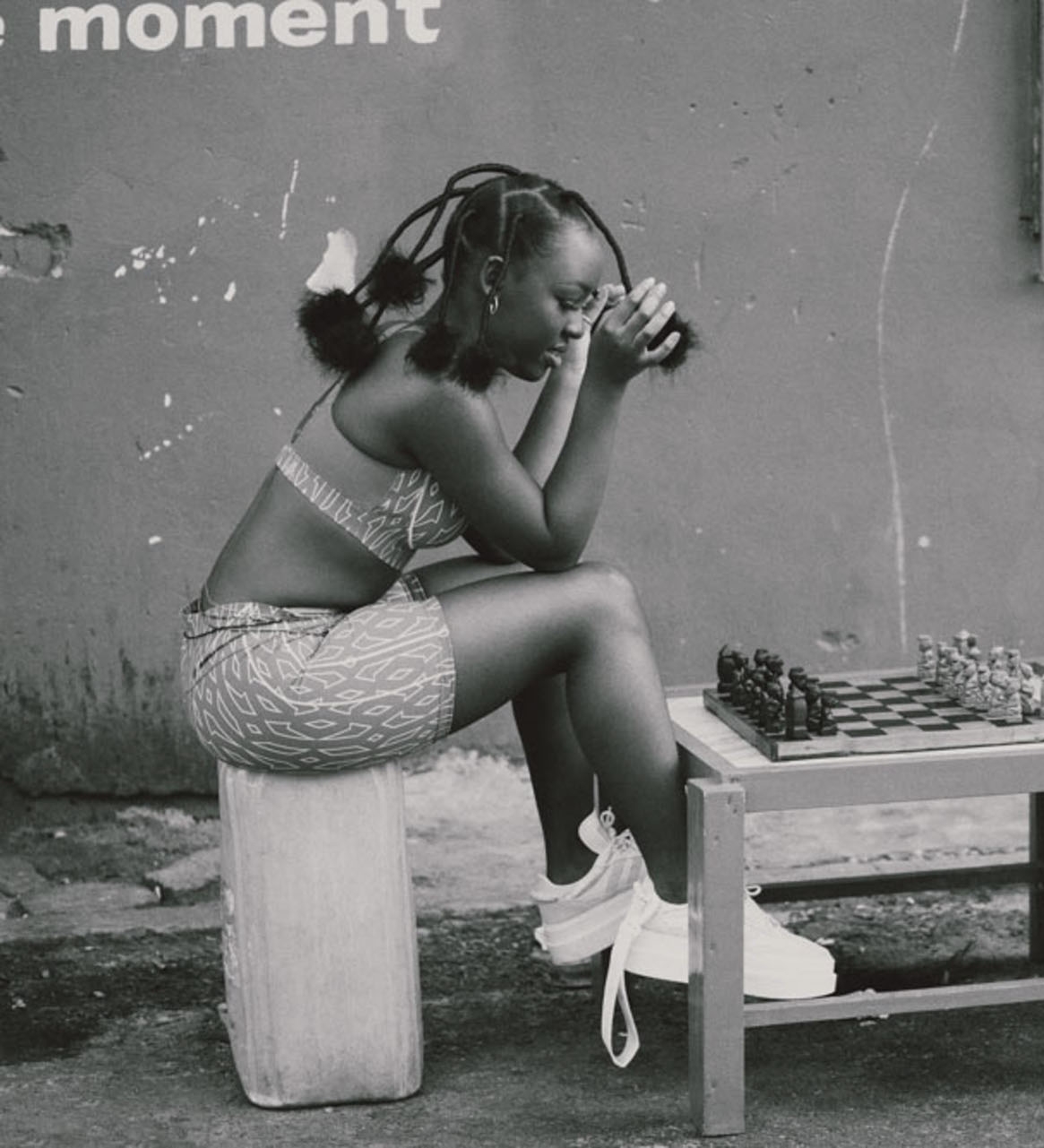Elsa Majimbo seated in front of a chessboard outdoors, black-and-white portrait