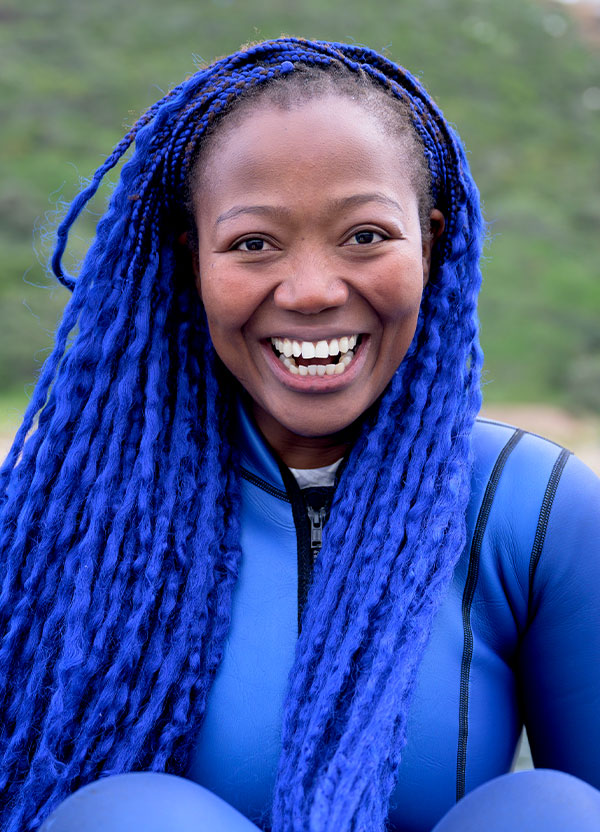Zandile Ndhlovu sourit, en combinaison bleue et avec de longues tresses bleues